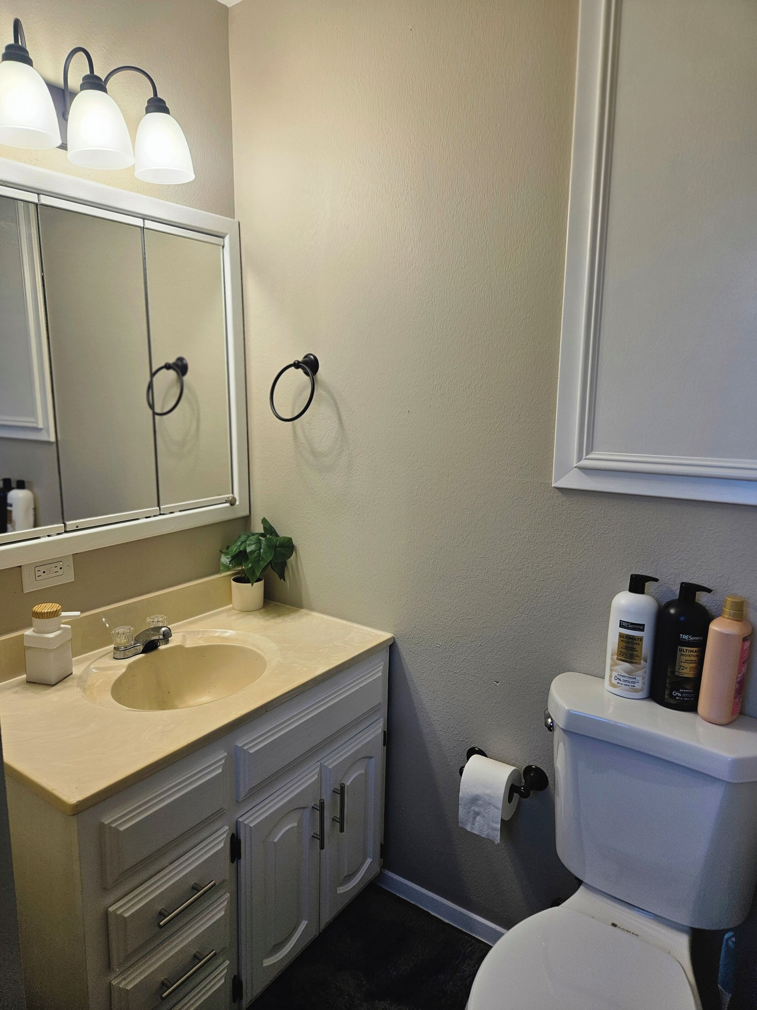 Une salle de bain avec un lavabo beige, un miroir, des toilettes et des articles de toilette accrochés au mur.