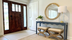 A hallway with a wooden door, a console table with a mirror, and a bench. - Cape Cod Charm -- Steps From Beach, 3 King Beds, Beach Equipment & Linens (Lewes)