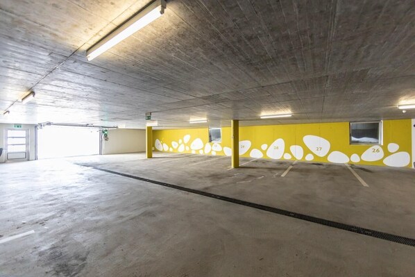 Un parking intérieur avec des planchers en béton et des murs jaunes ornés de formes abstraites blanches.