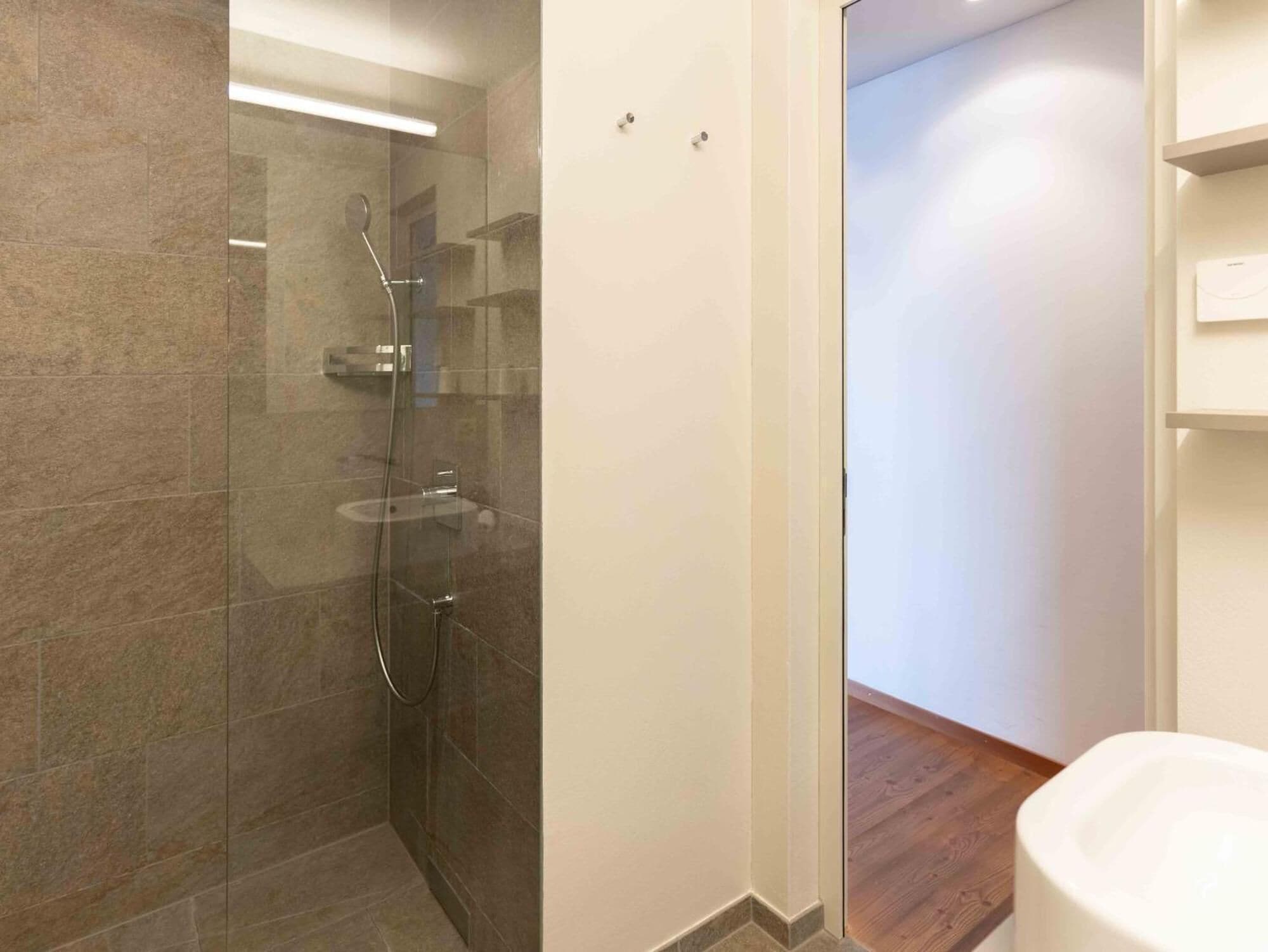 A modern bathroom with a glass-enclosed shower, a toilet, and a wooden floor.
