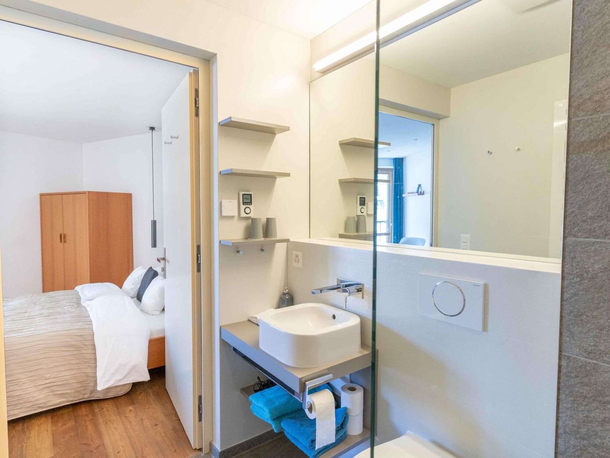 Quarto de hotel moderno com uma cama, um banheiro com pia e um espelho grande.