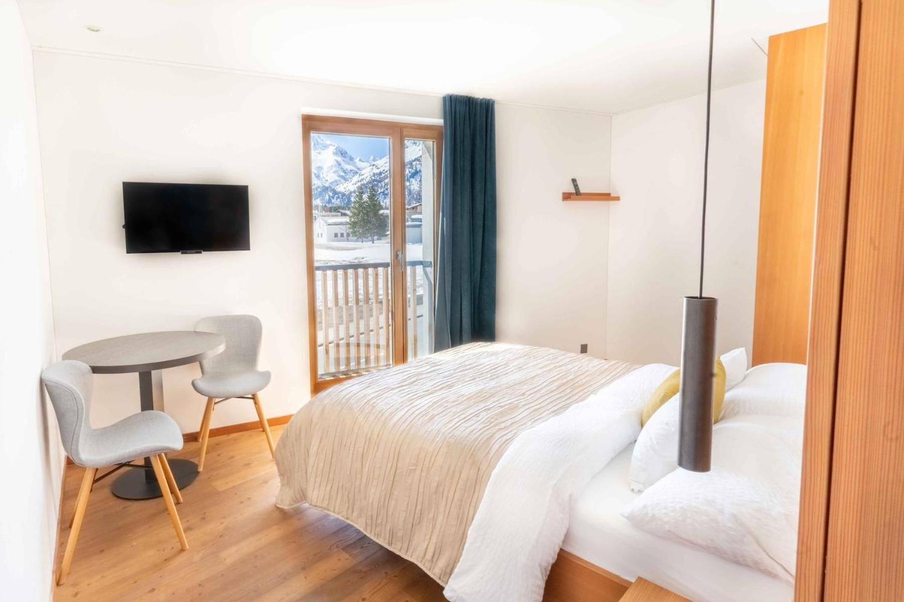 Une chambre d’hôtel comprenant un lit, un bureau avec une chaise, une télévision et un balcon offrant une vue sur des montagnes enneigées.