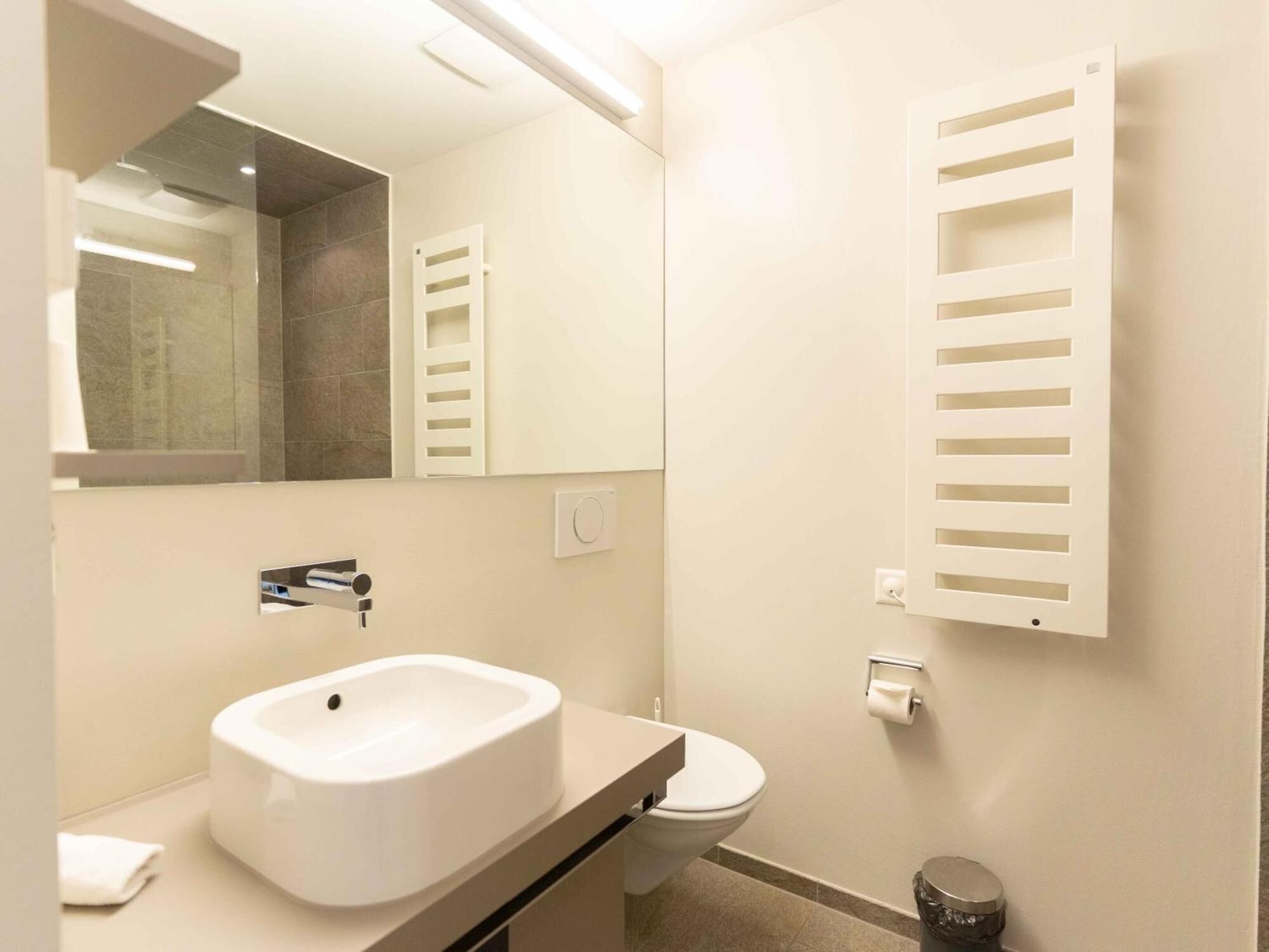 A modern bathroom with a white sink, toilet, and towel rack.