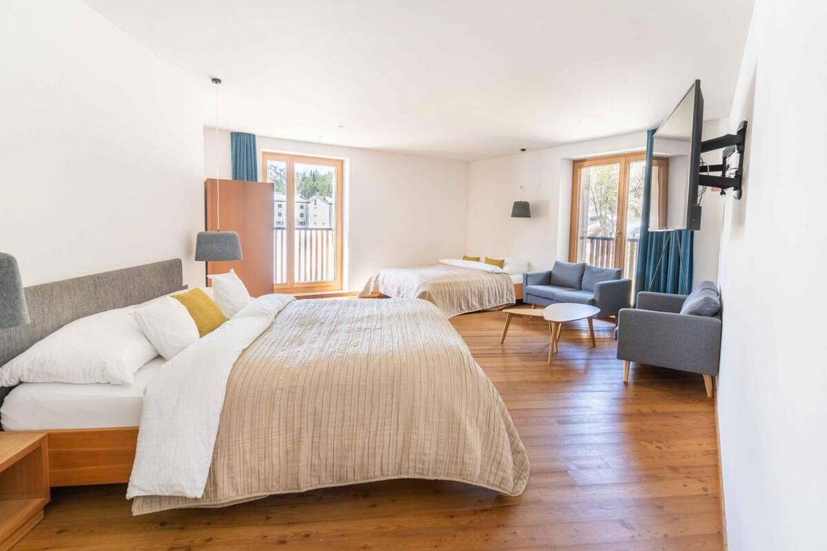 A hotel room with two beds, a sofa, a small table, and a TV.