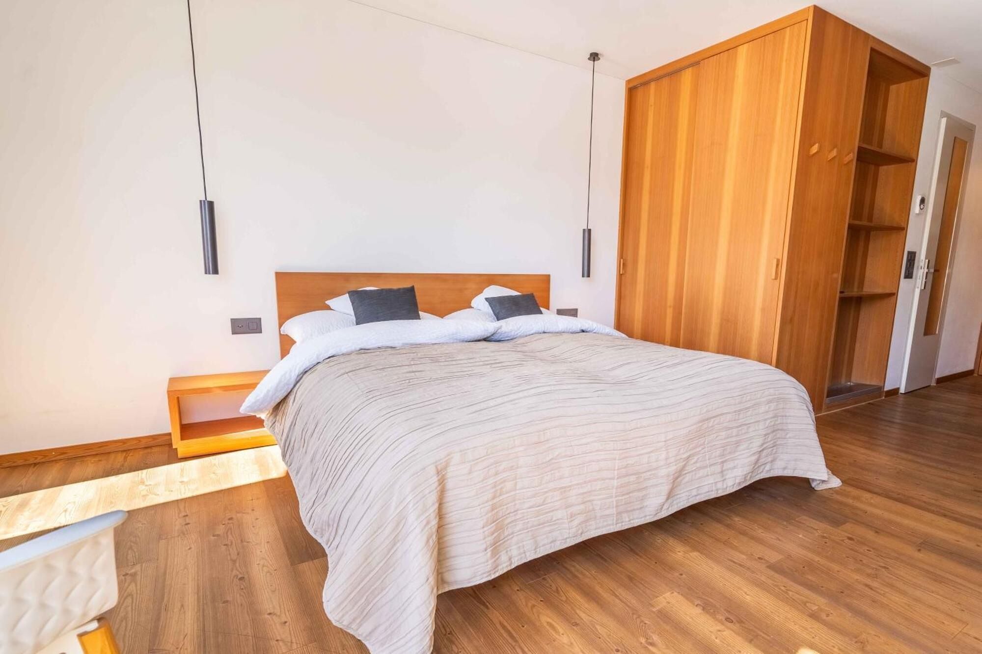A modern bedroom with a wooden bed, a nightstand, and a wardrobe.
