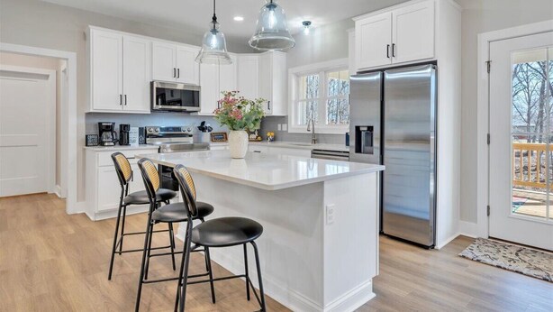 Una cocina moderna con armarios blancos, un refrigerador de acero inoxidable, una isla grande con taburetes de bar e iluminación colgante.