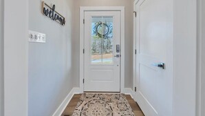Un pasillo con una puerta blanca, un cartel de bienvenida y una alfombra estampada.