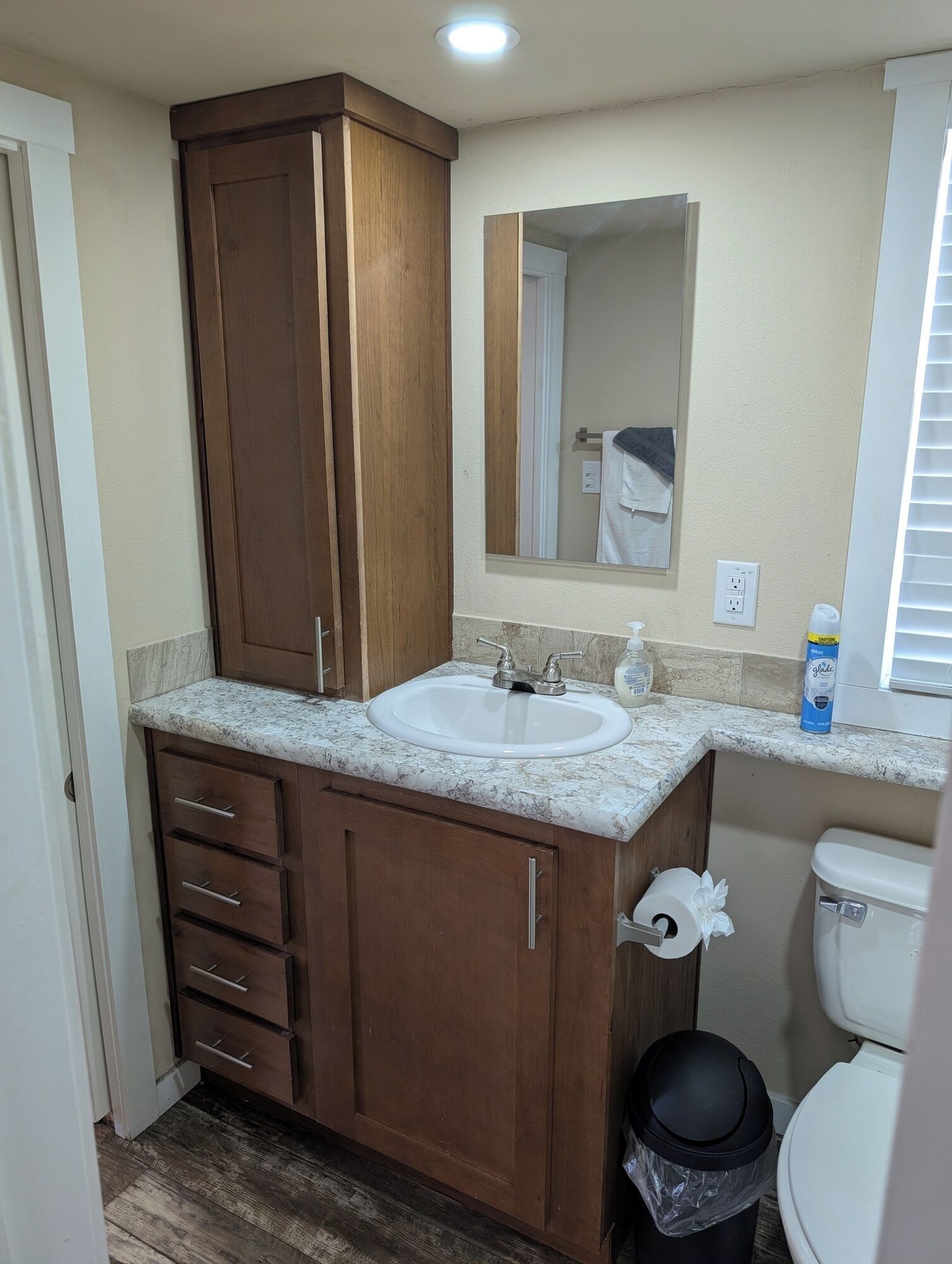A bathroom with a wooden vanity, a white sink, a mirror, and a toilet.
