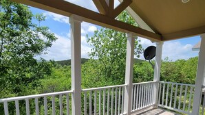 Eine Holzterrasse mit weißen Geländern, einer Satellitenschüssel und Blick auf grüne Bäume und Hügel.