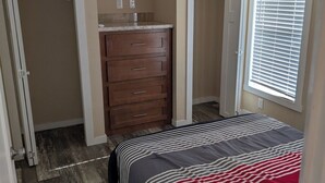 Ein Schlafzimmer mit Bett, Kommode, Kleiderschrank und einem Fenster mit Jalousien.