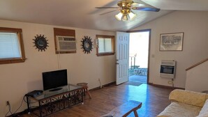 A living room with a wooden floor, a glass coffee table, a sofa, a TV on a stand, and a ceiling fan. - Mountain View 2 Bed Cabin (Davis)