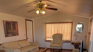 A living room with a sofa, armchair, wooden coffee table, ceiling fan, and a television on a wooden stand. - Mountain View 2 Bed Cabin (Davis)