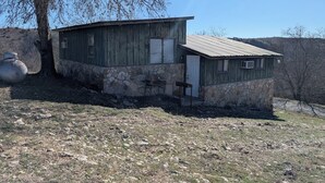 A rustic wooden building with a stone foundation, a metal door, and a small porch area. - Mountain View 2 Bed Cabin (Davis)