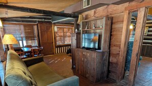 A rustic interior with a sofa, wooden walls, a television, and a dining area. - Family cabin w/large fireplace (Davis)
