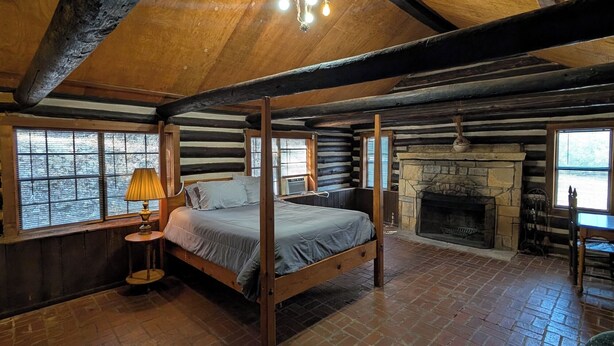 A log cabin bedroom with a four-poster bed, a stone fireplace, and large windows. - Family cabin w/large fireplace (Davis)