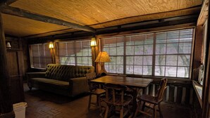 A cozy room with a wooden ceiling, a green sofa, a wooden table with chairs, and large windows with blinds. - Family cabin w/large fireplace (Davis)