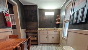 A kitchen with a wooden table and chairs, a window, and a trash can. - The Most Beautiful Views in Turner Falls (Davis)