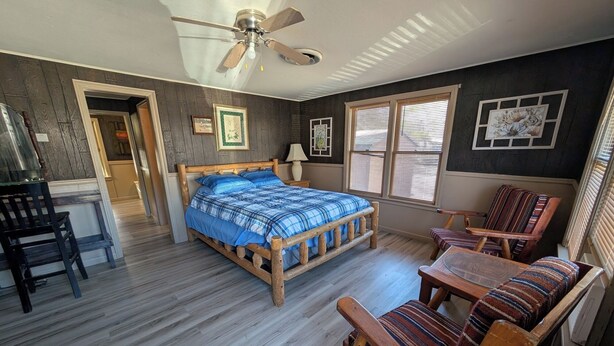 A bedroom with a wooden bed, a ceiling fan, a window with blinds, and a chair with a striped cushion. - The Most Beautiful Views in Turner Falls (Davis)