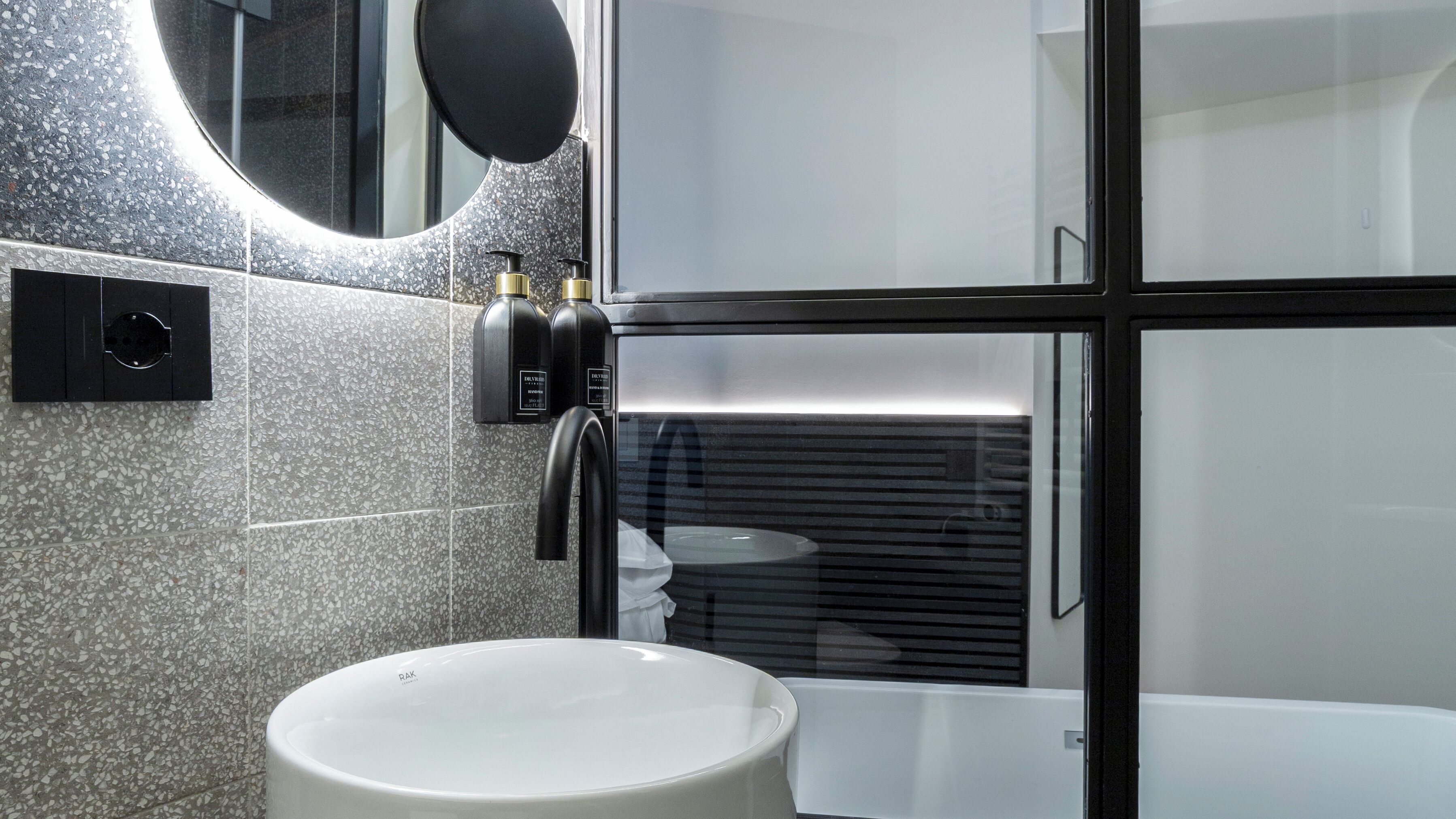 A modern bathroom with a round sink, a black faucet, a mirror, and a shower area.