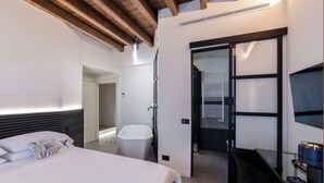 Une chambre d’hôtel moderne, dotée d’un grand lit, d’un bureau, d’une chaise, d’une baignoire et d’un téléviseur fixé au mur.