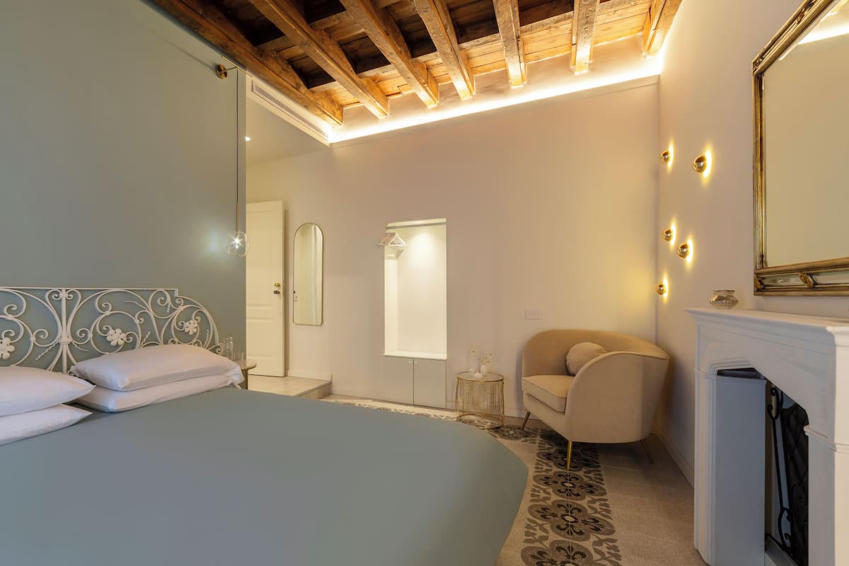 Une chambre à coucher avec un lit, une chaise, un miroir et une cheminée.