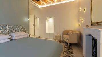 A bedroom with a bed, a chair, a mirror, and a fireplace.