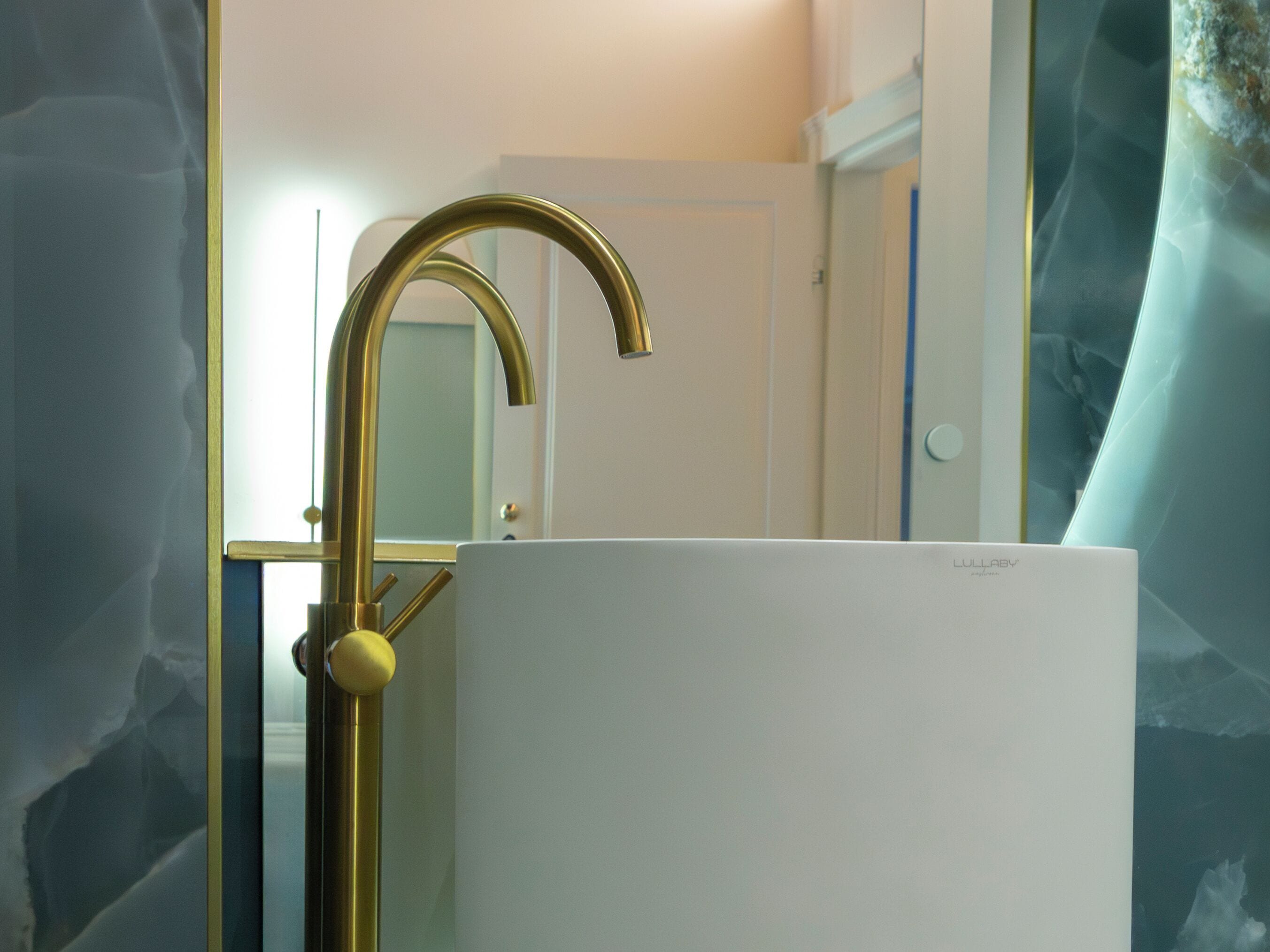Un baño con un lavamanos blanco, un grifo dorado y un espejo.