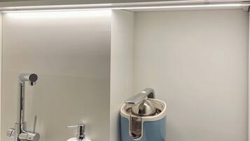A modern bathroom with a stainless steel sink, a soap dispenser, a blue vintage-style electric toothbrush, and a glass shower enclosure.
