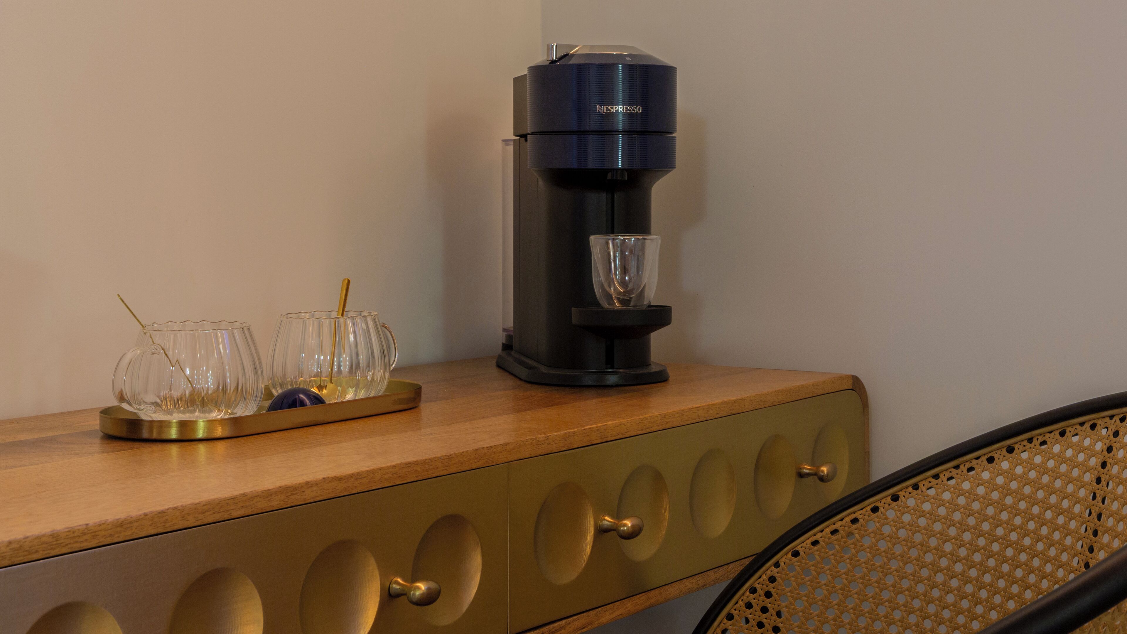 Una cafetera sobre una encimera de madera, con tres vasos de vidrio y una cuchara.