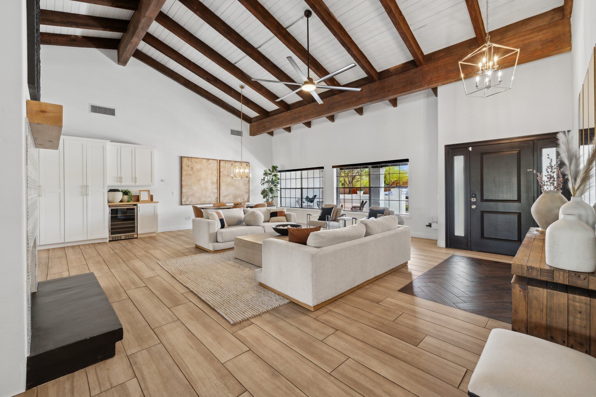 Un vaste salon doté d’un haut plafond, de poutres apparentes et d’une grande fenêtre. On y trouve un ensemble de canapés, une table basse et un tapis sur le plancher en bois.