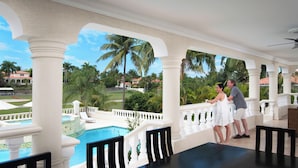Un espacio exterior cubierto con piscina, columnas blancas y vista a un paisaje tropical.