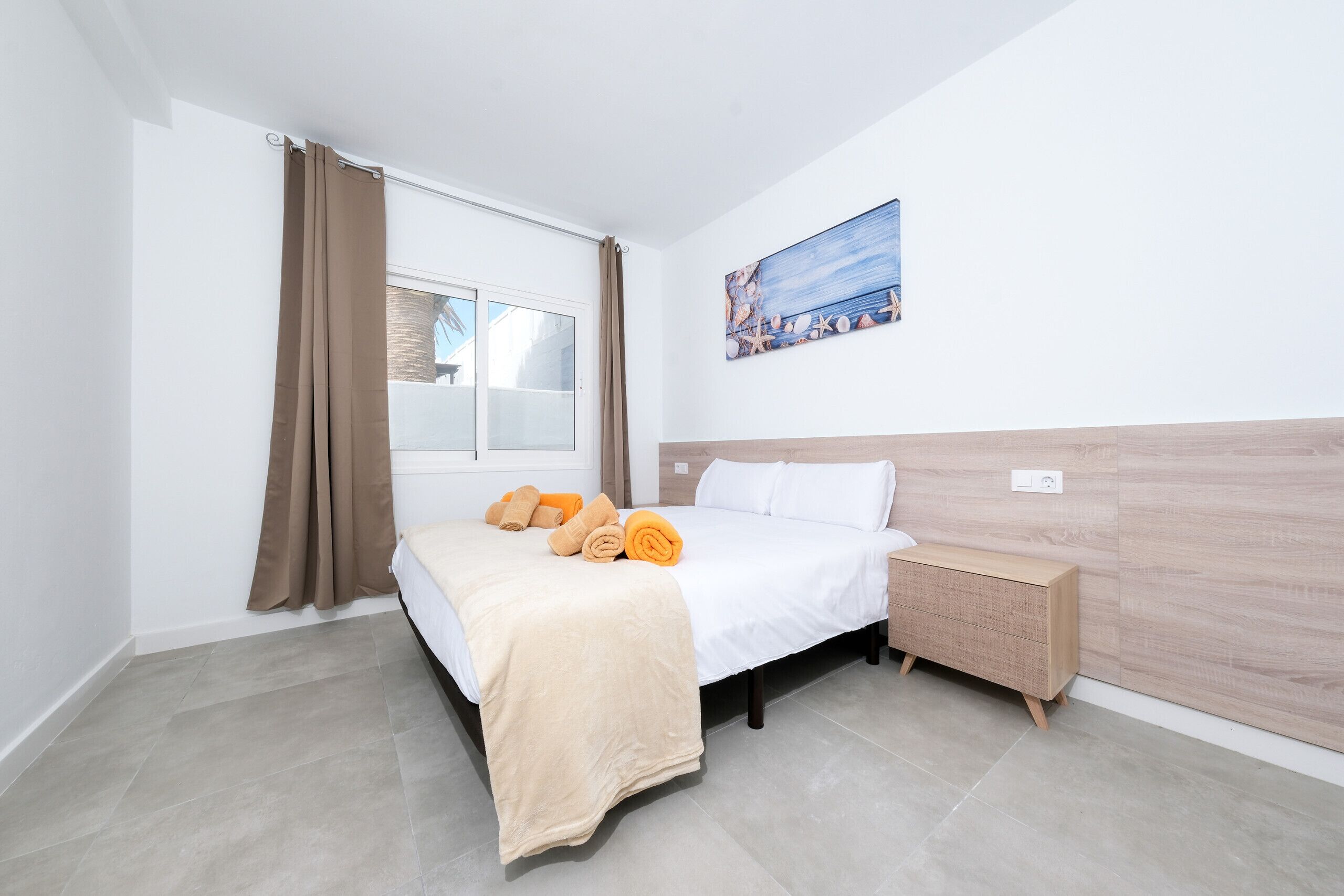 Une chambre d’hôtel avec un lit, une table de chevet, une fenêtre avec des rideaux et un tableau au mur.