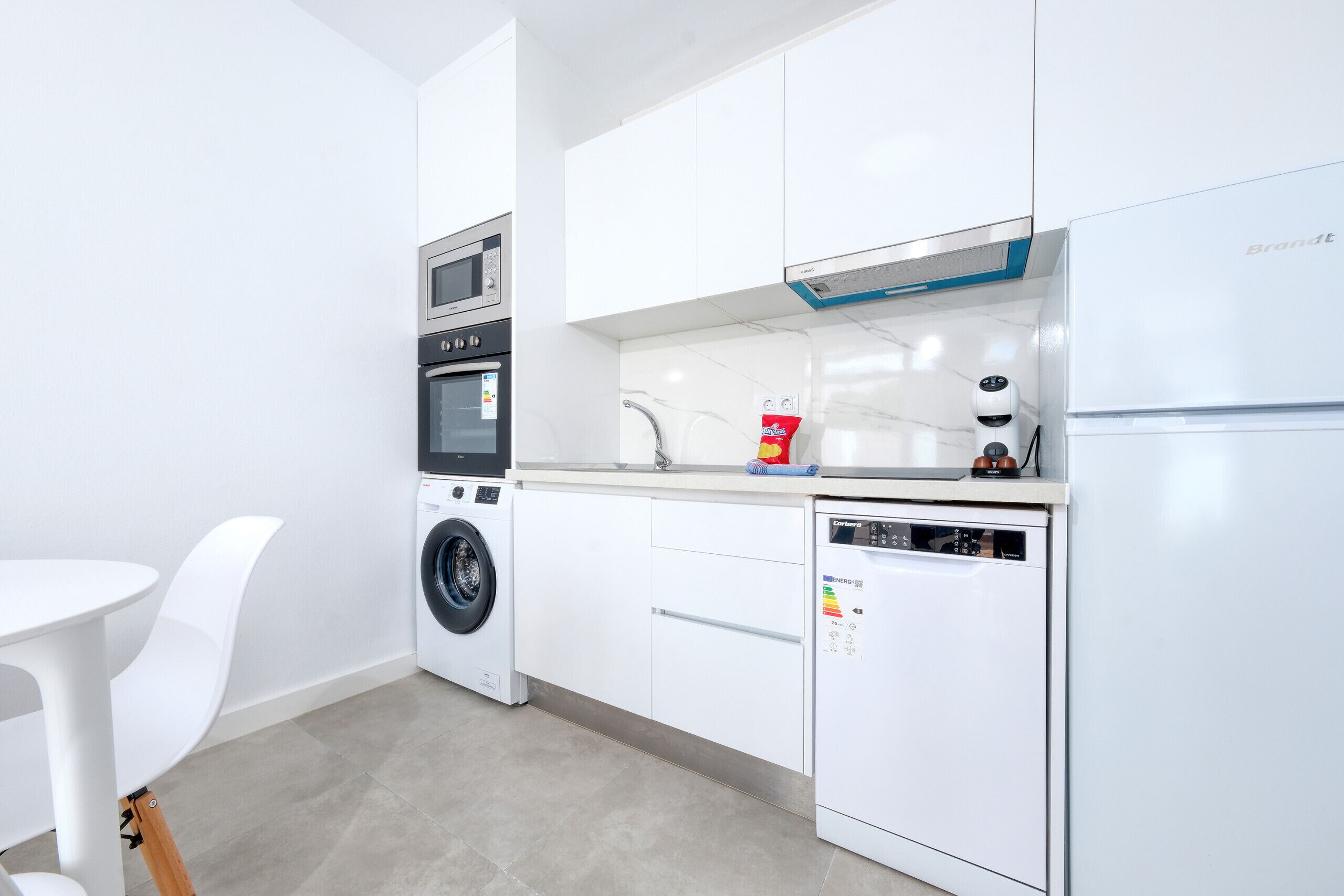 Een moderne keuken met witte kasten, een inbouwoven, een vaatwasser en een koffieapparaat.