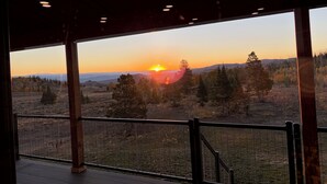 Vista al atardecer desde un espacio exterior cubierto con terraza de madera y barandilla de metal.