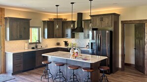 Una cocina moderna con armarios de madera oscura, una isla central con taburetes, electrodomésticos de acero inoxidable e iluminación colgante.