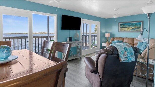 A living room with a view of the water, a dining area with a table and chairs, and a bedroom with a bed and a lamp. - MANATEE COTTAGE:  Gulf Front 2-bedroom house (Hudson)