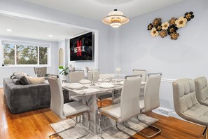Un espace repas moderne avec une table en marbre, des chaises blanches et un grand écran de télévision affichant le logo de Netflix.