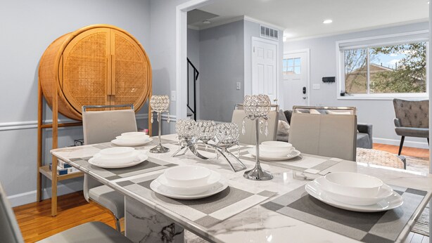 Un coin repas avec une table dressée pour quatre personnes, une chaise en osier et une vue sur l’extérieur par une fenêtre.