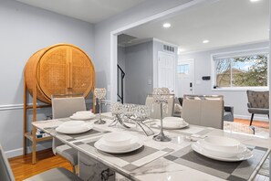 A dining area with a table set for four, a wicker chair, and a view of the outdoors through a window. - Modern 4BR Getaway 3 Min to Old Town 1 Mil to Waterfront Walk to Metro (Alexandria)