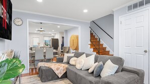 Un salon moderne avec un canapé d’angle gris, un escalier en bois et un coin repas à l’arrière-plan.