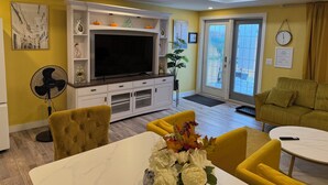 A living room with a flat-screen TV, yellow walls, a dining table with chairs, a sofa, and a fan. - HOME AWAY FROM HOME (Winnipeg)