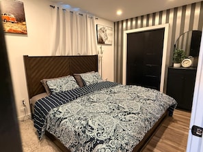 Un dormitorio con una colcha estampada, un cabecero, una puerta, un espejo y un cuadro colgado en la pared.