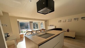 Une cuisine moderne avec un îlot central, un coin repas avec des chaises et une vue par la fenêtre.