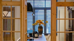 A modern kitchen with a central island, wooden cabinetry, and a large window with blinds. - Circa 1929 - Suite met keuken (Ostend)
