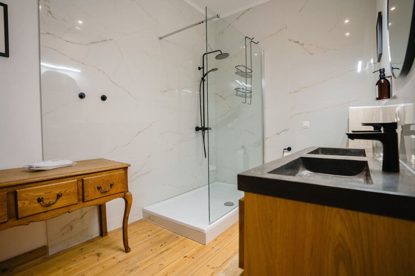 Een moderne badkamer met een glazen douchecabine, een houten wastafelmeubel met een wastafel en een wand betegeld met marmer.
