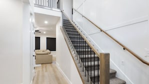 Een modern interieur met een trap, houten vloeren en een beige bank op de achtergrond.