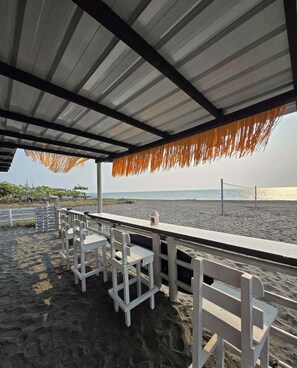 Uma área de estar à beira-mar com cadeiras brancas e uma mesa, com vista para o oceano.