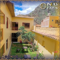 Un edificio amarillo con patio, un pequeño jardín y una montaña al fondo.