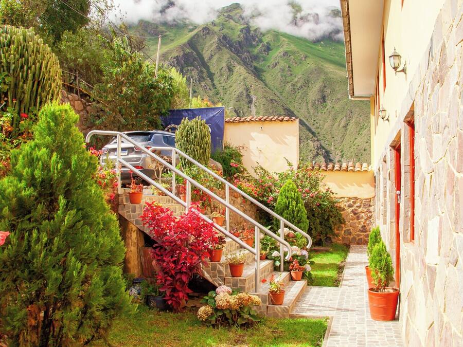Un patio con una escalera de piedra que conduce a un edificio, rodeado de macetas con plantas y un coche aparcado cerca.