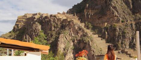Una persona de pie en un balcón con vistas a ruinas antiguas en una montaña.